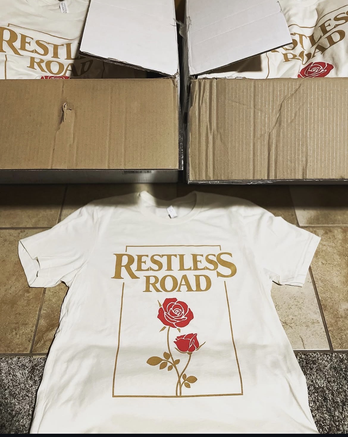 Restless Road white band tee with gold typography and red rose design